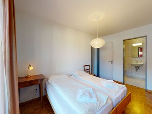 Ein Hotelzimmer mit Bett, Nachttisch, Lampe und einem durch eine offene Tür einsehbaren Badezimmer.