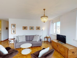 Ein Wohnzimmer mit einer Couch, zwei Sesseln, einem Couchtisch, einem Fernseher und einer Kristallleuchter.