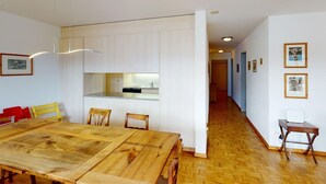 A spacious dining area with a wooden table and chairs, a kitchen in the background, and a hallway leading to other rooms. - Apartment Crappun 3 by Interhome (Samedan)
