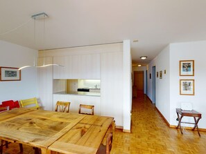 Ein geräumiger Essbereich mit Holztisch und Stühlen, im Hintergrund eine Küche und ein Gang zu weiteren Räumen.