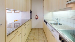 A narrow kitchen with light-colored cabinets, a granite countertop, and a tiled backsplash. - Apartment Crappun 3 by Interhome (Samedan)