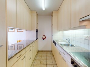 Eine schmale Küche mit hellen Schränken, einer Granit-Arbeitsplatte und einer gefliesten Rückwand.