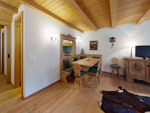 Ein Essbereich mit Holztisch und -stühlen, eine Holzkommode mit Fernseher und ein Kuhfellteppich auf dem Boden.