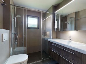 A modern bathroom with a glass shower enclosure, a toilet, and a vanity with a mirror. - Apartment Larschigna - Attraktive 3.5-Zimmerwohnung by Interhome (Zuoz)