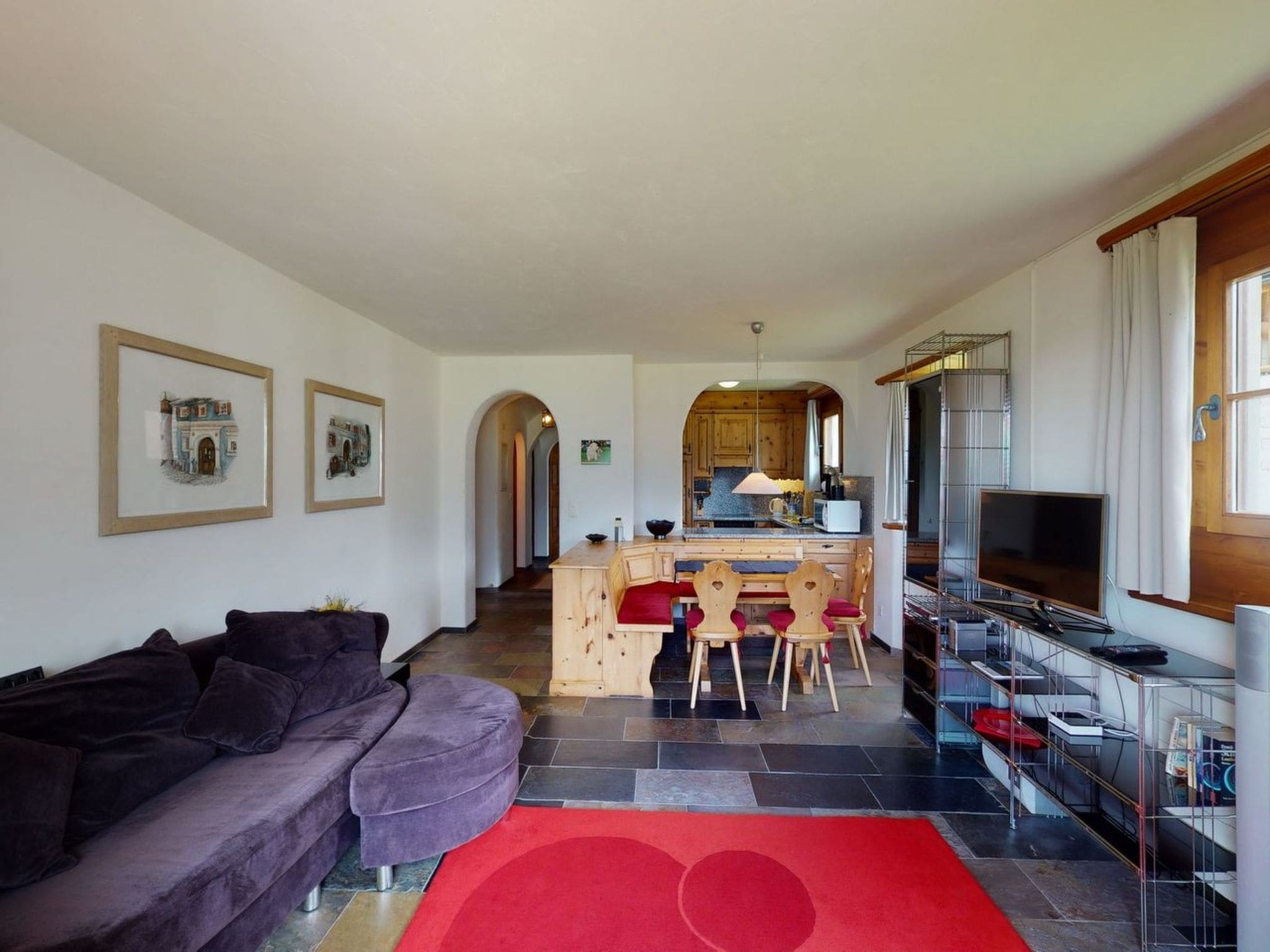 A living room with a sofa, a red rug, and a kitchen area with a dining table and chairs.
