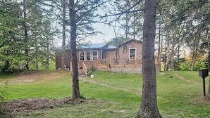 Une cabane en bois dotée d’une terrasse et d’une cour clôturée, entourée d’arbres.