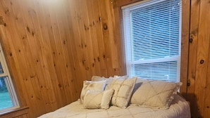 Un lit avec une couverture matelassée et des oreillers, des murs en bois et une fenêtre avec des stores.