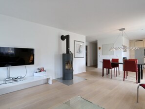 A modern living room with a flat-screen TV, a black fireplace, and a dining area with red chairs. - Apartment Falcun by Interhome (Celerina)