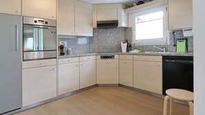 Eine moderne Küche mit Einbauofen, Mikrowelle und Geschirrspüler, hellen Schränken, Granit Arbeitsplatten und einem Fenster für natürliches Licht.