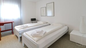 Ein Hotelzimmer mit zwei Einzelbetten, einem Schreibtisch, einem Stuhl, einer Lampe und zwei gerahmten Bildern an der Wand.