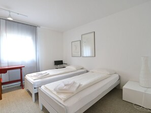 A hotel room with two single beds, a desk, a chair, a lamp, and two framed pictures on the wall. - Apartment Falcun by Interhome (Celerina)