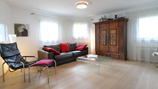 Ein Wohnzimmer mit einer Ledersofa, einem Glastisch, einer Holzkommode und einem schwarzen Sessel.