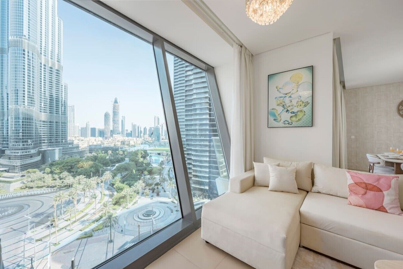 A modern living room with a large window offering a city view, a sofa with cushions, and a chandelier.