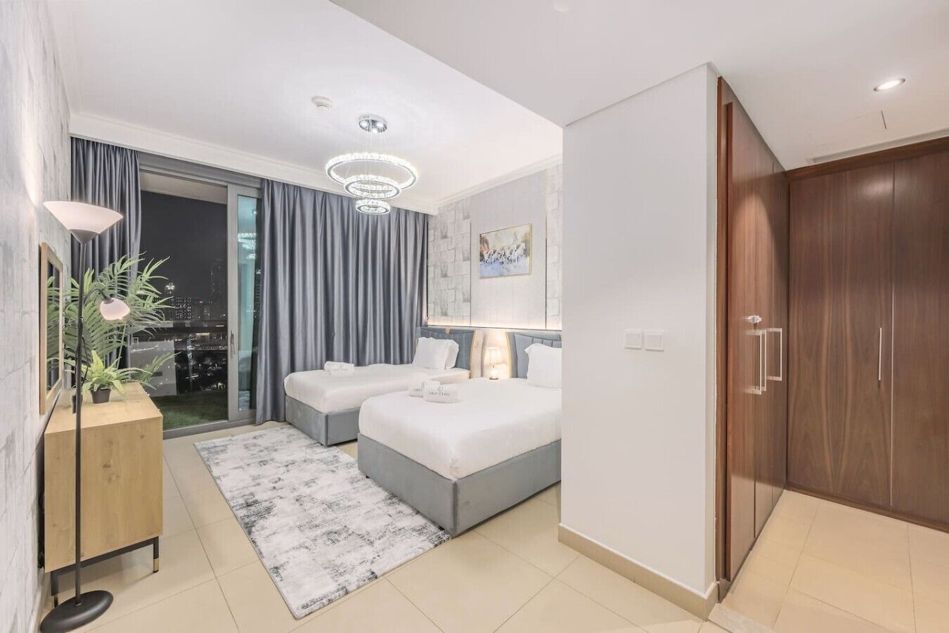 Habitación de hotel moderna con una cama grande, un escritorio, una silla y vistas de la ciudad por la noche.