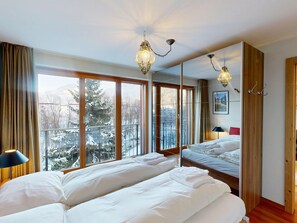 Ein Hotelzimmer mit zwei Betten, großen Fenstern und Blick auf schneebedeckte Bäume.