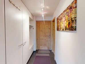 Ein Flur mit einer Holztür, einer weißen Wand mit einem farbenfrohen Gemälde und einem gefliesten Boden.