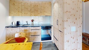 Une cuisine moderne avec des meubles en bois, un four encastré et un coin repas comprenant une table et des chaises en bois.
