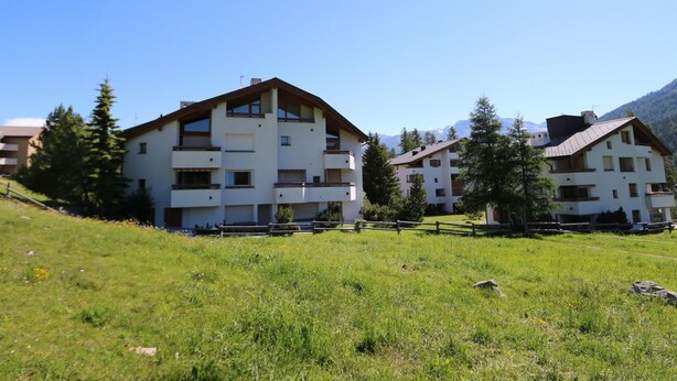 Un immeuble à plusieurs étages doté de balcons, entouré de verdure et de montagnes.