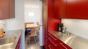 Eine kompakte Küche mit roten Schränken, Edelstahl-Arbeitsflächen, einer Kaffeemaschine und einem Holztisch mit Stühlen.