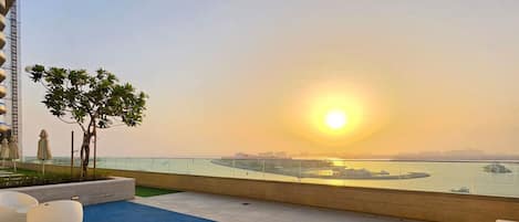 Une terrasse sur le toit offrant une vue sur le coucher de soleil sur l’eau, avec des sièges modernes et un petit arbre.