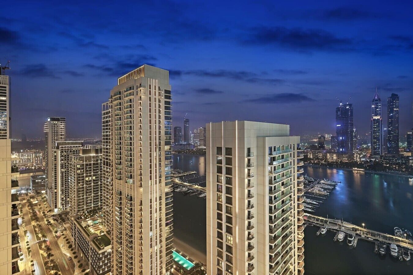 Un edificio de gran altura con varios pisos, una marina con barcos y el perfil del horizonte urbano al fondo.
