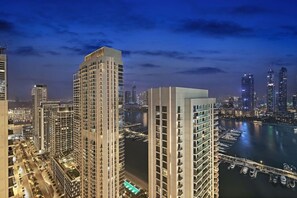 A high-rise building with multiple floors, a marina with boats, and a city skyline in the background. - FIRST CLASS |1BR| Beachfront with Ain Dubai Views (Dubai Harbour)
