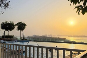Un espace piscine avec des chaises longues et une vue sur le coucher de soleil au-dessus d’une étendue d’eau.