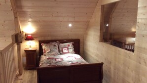 Quarto com estrutura de madeira, uma cama, mesa de cabeceira, abajur e janela.