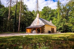 A rustic cabin with a chimney, wooden porch, and a stone foundation, surrounded by a forested area. - Maison du Garde Forestier au cœur des Châteaux de la Loire (Cour-Cheverny)