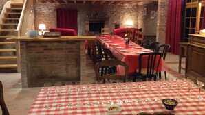 Um restaurante com uma longa mesa de jantar posta para uma refeição, paredes de pedra e uma escada de madeira.
