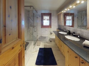 Un baño moderno con cabina de ducha de vidrio, dos lavamanos y un espejo grande.