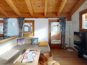 A cozy cabin interior with a wooden ceiling, a sofa with patterned cushions, a television, and a window with curtains. - Apartment Stalla Bodmer by Interhome (Samedan)