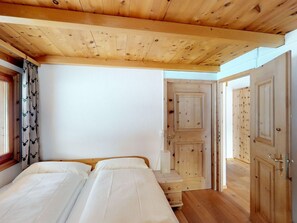 Habitación con dos camas, techo de madera y puertas que dan a otras áreas.