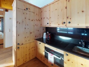 A kitchen with wooden cabinets, a black countertop, a sink, a dishwasher, and a stove. - Apartment Stalla Bodmer by Interhome (Samedan)