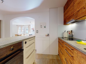 A modern kitchen with wooden cabinets, a granite countertop, and a view into the dining area. - Apartment Promulins B4 by Interhome (Samedan)