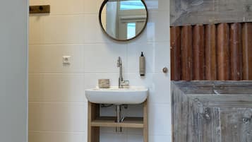 Ein Badezimmer mit einem weißen Waschbecken, einem runden Spiegel und einem Holzregal.
