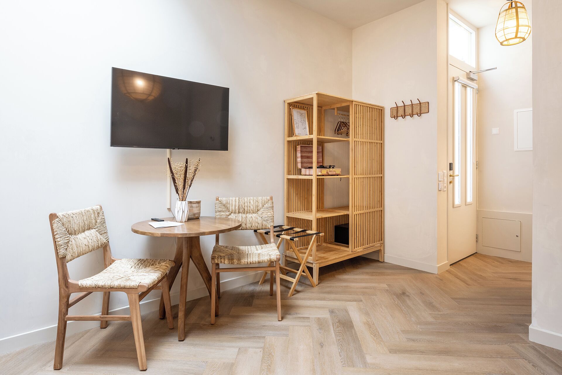 Une pièce comprenant une table ronde en bois, quatre chaises en osier, une bibliothèque et un téléviseur fixé au mur.