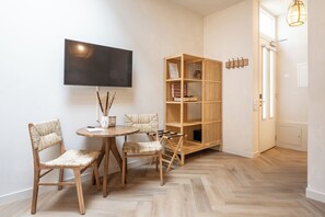Een kamer met een ronde houten tafel, vier rieten stoelen, een boekenkast en een aan de muur bevestigde televisie.