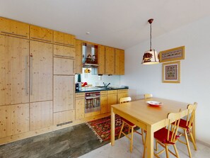 A kitchen with wooden cabinets, a dining table with chairs, and a hanging light fixture. - Apartment Sur Puoz 2A by Interhome (Samedan)