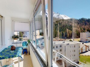 Ein Balkon mit Tisch und Stühlen, einem Blumentopf und Blick auf schneebedeckte Berge und bewaldetes Gebiet.