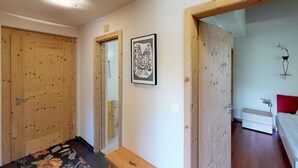 Un pasillo con puertas de madera, un banco, un cuadro enmarcado y una cama en la habitación contigua.
