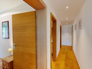 Un couloir doté d’un plancher en bois, de murs blancs et d’une porte située sur le côté gauche.