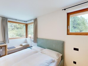 A bedroom with a bed, a bedside table, a lamp, and a window with curtains. - Apartment Margnetta by Interhome (Maloja)
