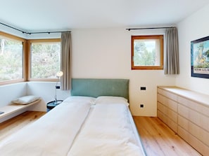 A bedroom with a bed, bedside table, lamp, and a window with curtains. - Apartment Margnetta by Interhome (Maloja)