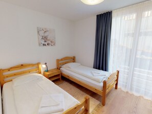 Una habitación con dos camas de madera, una mesita de noche con lámpara, un cuadro en la pared y una ventana con cortinas.