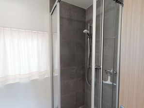 A glass-enclosed shower stall with a handheld showerhead and a wall-mounted faucet. - Apartment Randurel by Interhome (Zuoz)