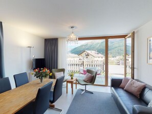 A modern living room with a dining area, large windows, and a view of a mountain landscape. - Apartment Randurel by Interhome (Zuoz)