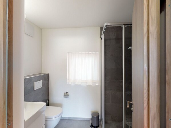 Baño con inodoro, ducha y ventana con cortina.