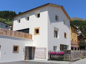 A two-story building with a white facade, a wooden balcony, and a gate with decorative elements. - Apartment Randurel by Interhome (Zuoz)