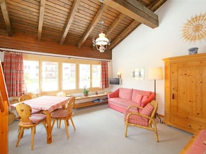 Una habitación acogedora con techo de madera, un sofá, una mesa de comedor con sillas y un televisor.